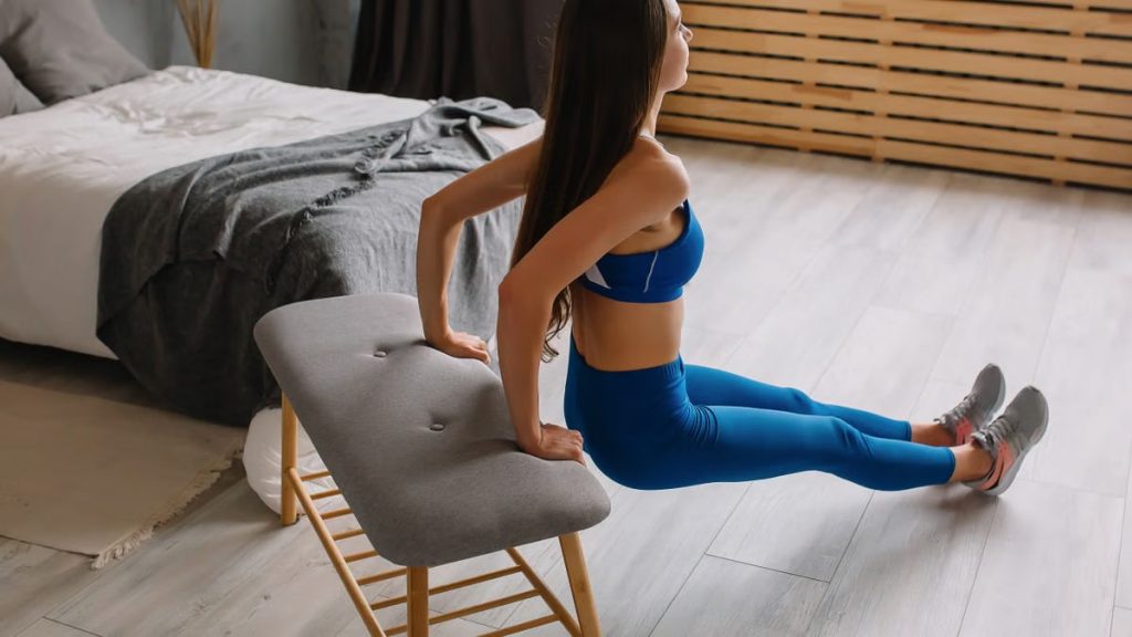 Young woman in sportswear doing tricep dips using bench at home.